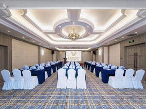 A conference room with rows of tables, white chairs, and a chandelier.