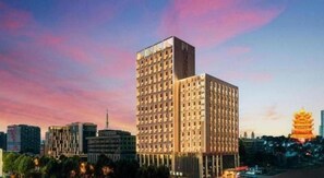 A high-rise building with a modern architectural design, surrounded by other buildings and a cityscape. - Vienna International Hotel (Wuhan Yellow Crane Tower Pengliuyang Subway Station) (Wuhan)