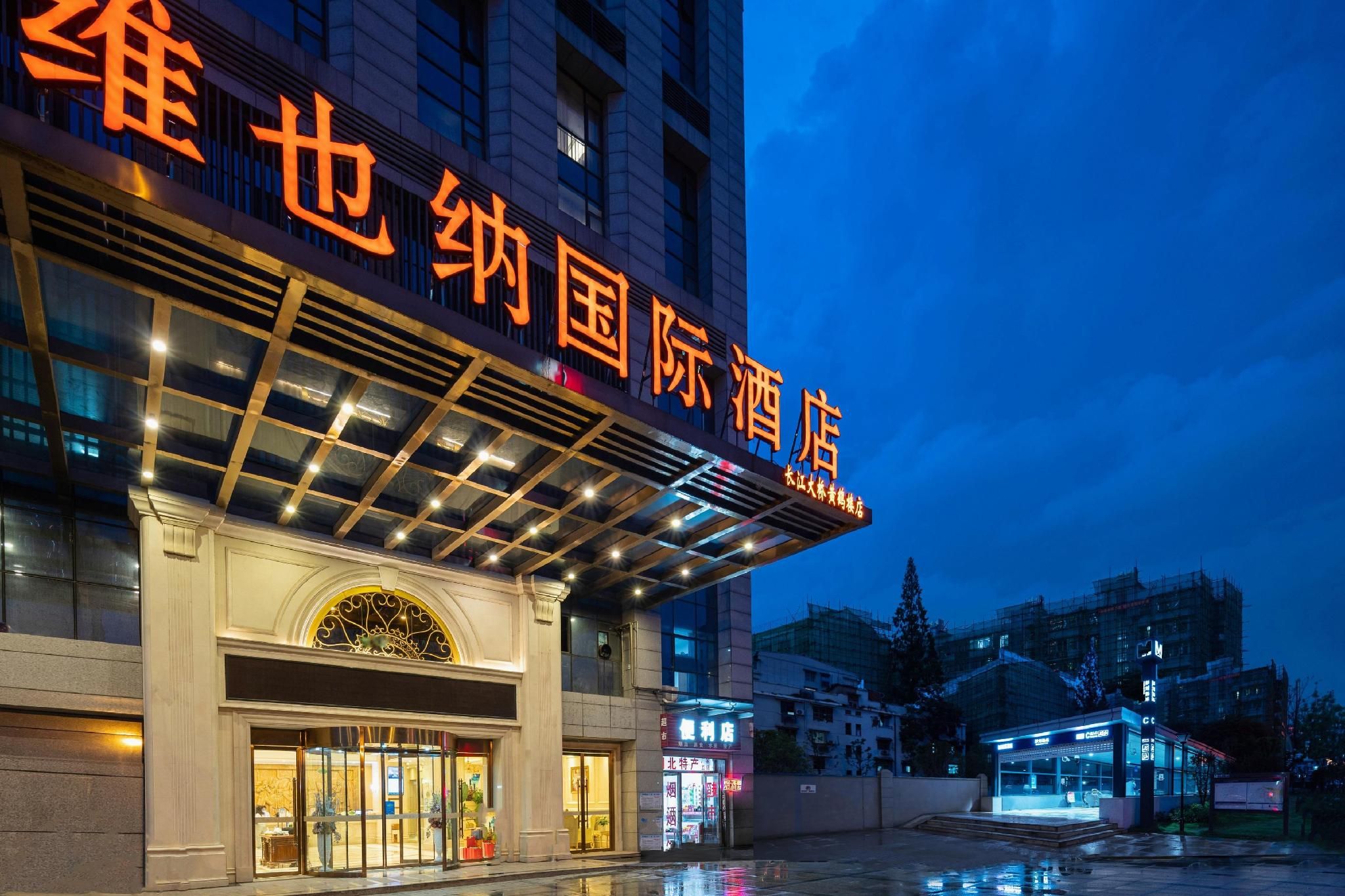 A hotel entrance with a large illuminated sign, a covered entrance area, and a wet ground reflecting lights.