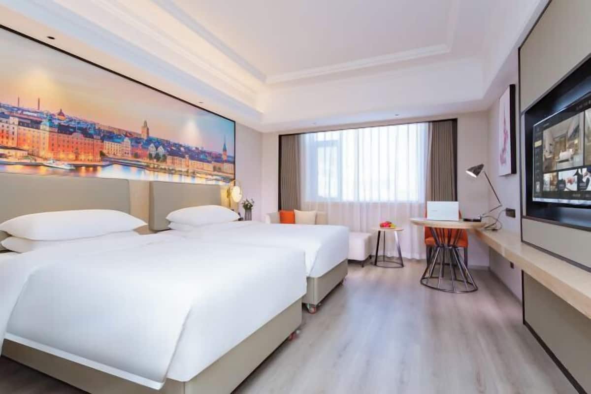 Une chambre d’hôtel avec deux lits, un bureau, une chaise, une télévision et une grande fenêtre.