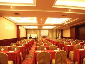 Une salle de conférence avec des rangées de tables et de chaises, un écran de projection et un sol recouvert de moquette.