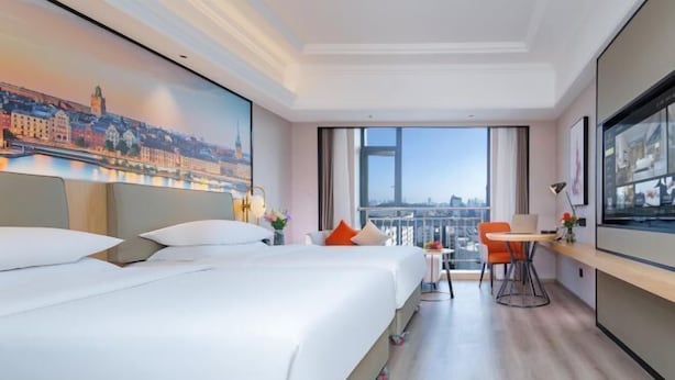 A hotel room with two beds, a desk, a chair, and a large window with a city view. - Vienna International Hotel (Wuhan Yellow Crane Tower Pengliuyang Subway Station) (Wuhan)