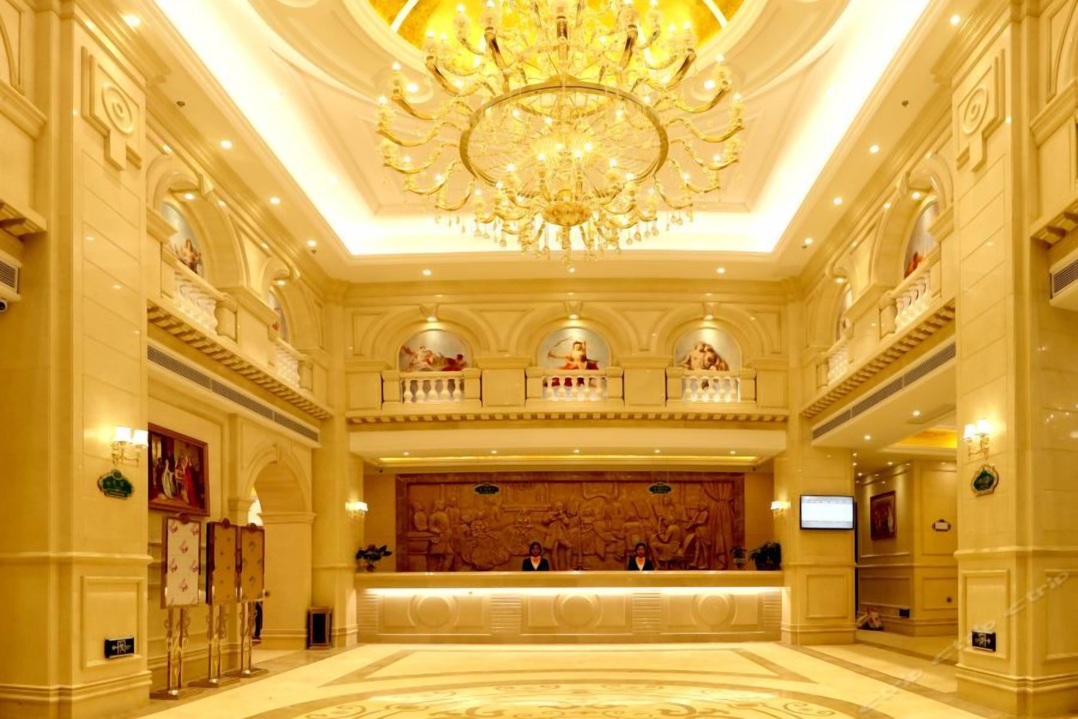 A grand lobby with a large chandelier, ornate wall decorations, and a reception desk.