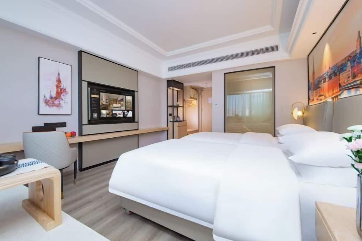 Une chambre d’hôtel moderne, dotée d’un grand lit, d’un bureau avec une chaise, d’une télévision et d’œuvres d’art accrochées aux murs.