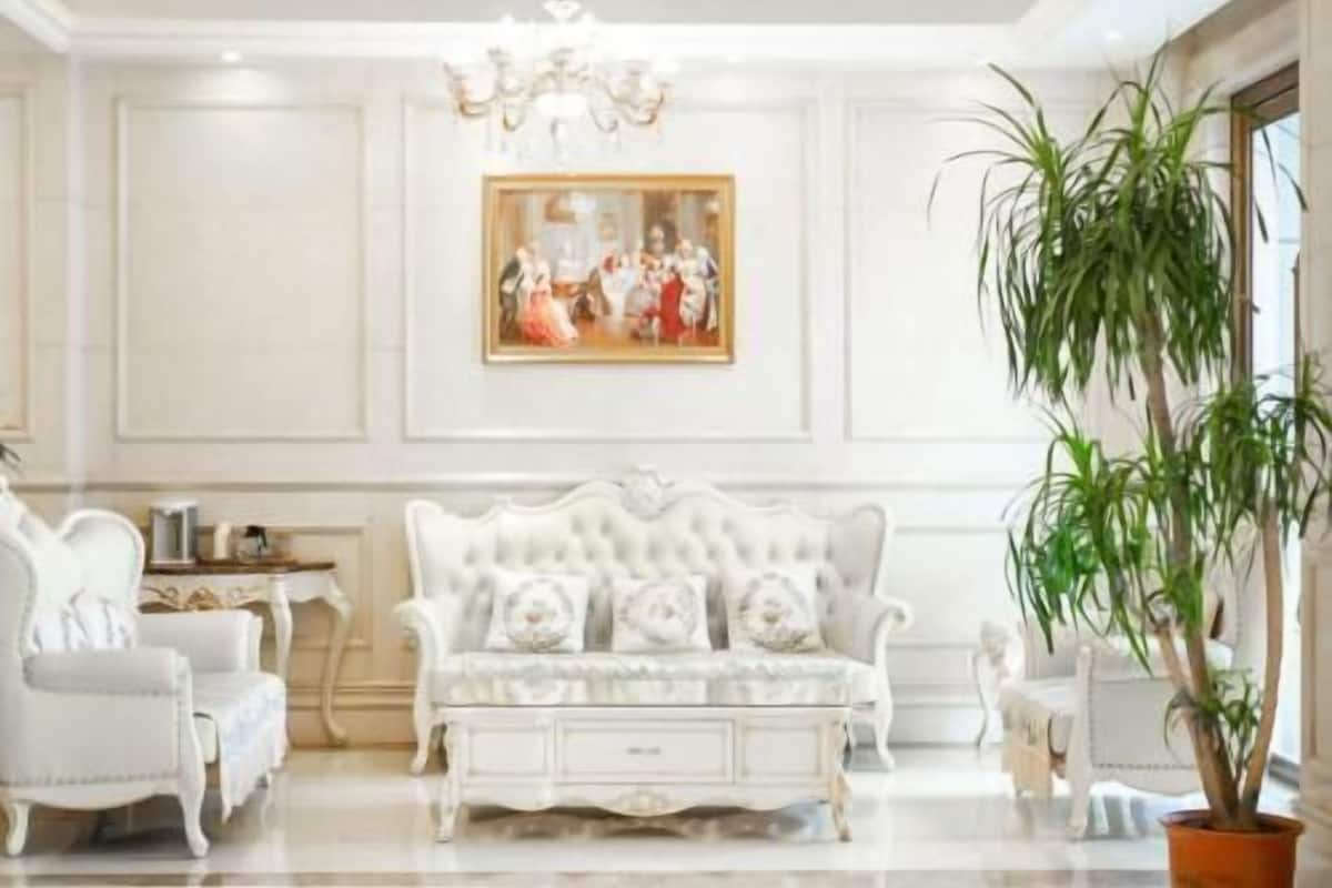 Une pièce avec un canapé blanc, deux fauteuils blancs, un lustre, un tableau encadré et une plante en pot.