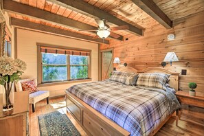 A wooden cabin bedroom with a bed, a bench, a window, and a ceiling fan.