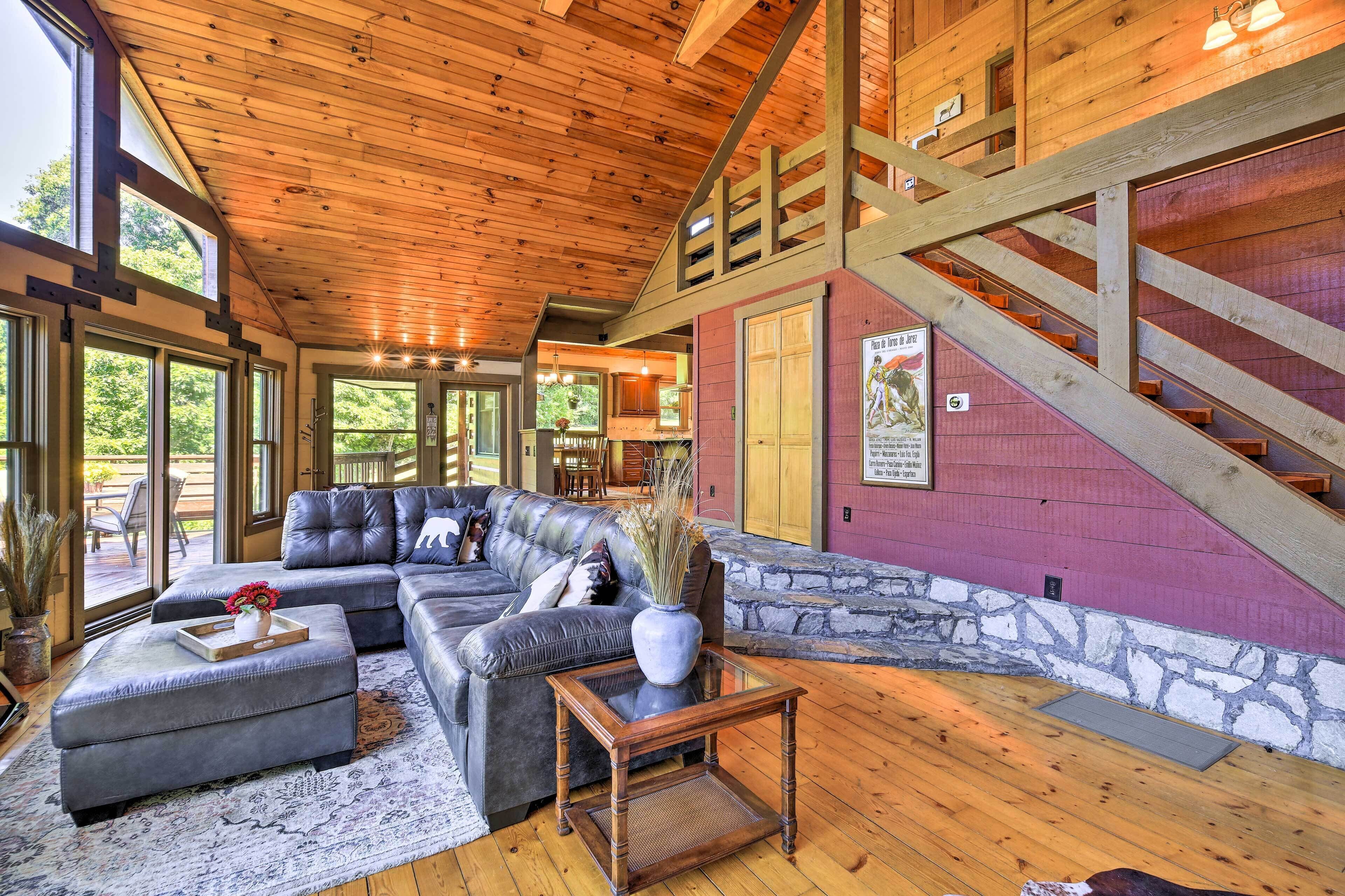 A spacious living room with a large sectional sofa, a glass coffee table, and a wooden staircase.
