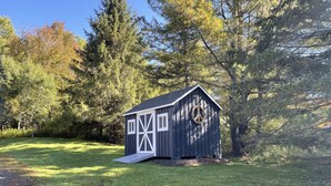 A small wooden shed with a sloped roof and white trim, situated on a grassy area with trees in the background. - Cozy year round retreat! Close to skiing, hiking and swimming. (East Jewett)