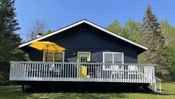 A two-story cabin with a balcony, a yellow door, and a white railing. - Cozy year round retreat! Close to skiing, hiking and swimming. (East Jewett)