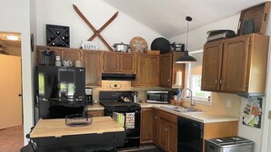 A compact kitchen with wooden cabinets, a black refrigerator, a stove, a microwave, and a dishwasher. There are two black bar stools at the counter. - Cozy year round retreat! Close to skiing, hiking and swimming. (East Jewett)