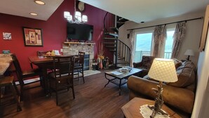 Un salon chaleureux avec une cheminée, un coin repas et un escalier menant à l’étage supérieur.