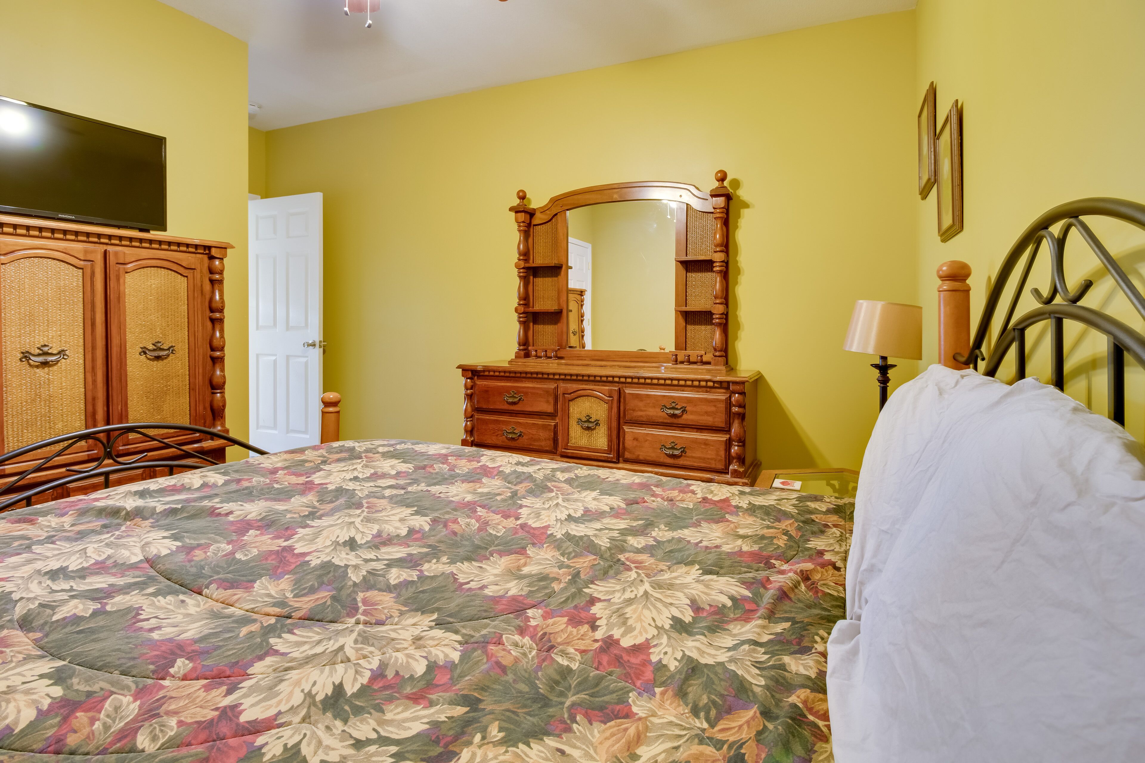 A bedroom with a floral bedspread, wooden dresser, and a mirror.
