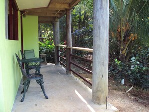 A covered outdoor area with a table and chairs, surrounded by greenery and a wooden fence. - Riversiedview House (Calibishie)