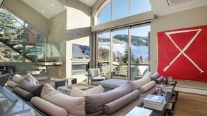 Una sala de estar moderna con un sofá seccional grande, una chimenea y un ventanal con vistas a la montaña.