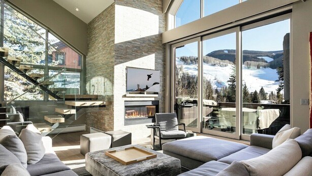 Amplia sala de estar con chimenea, ventanas grandes y vistas a un paisaje nevado.