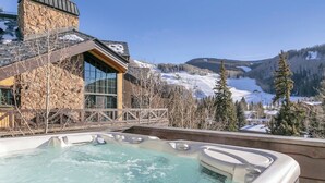 Un jacuzzi con vistas a la montaña, un edificio de piedra y laderas nevadas.