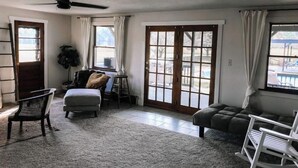 A spacious living room with a large window, a ceiling fan, and a cozy seating area. - Kennerdell Country Retreat with seasonal inground pool (Kennerdell)