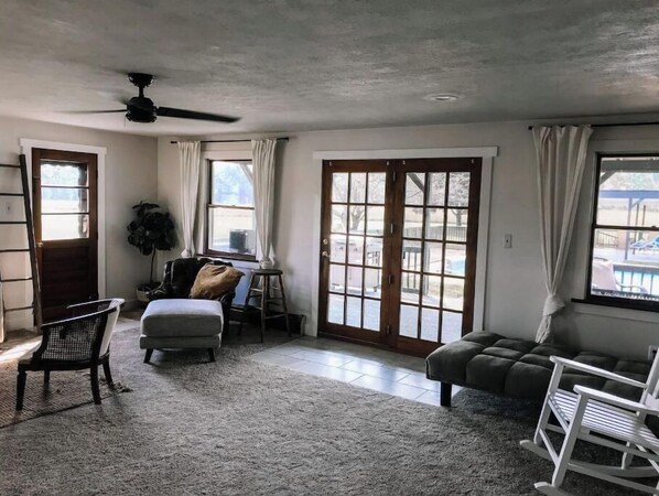 A spacious living room with a large window, a ceiling fan, and a cozy seating area.