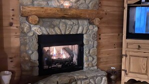 Ein Kamin aus Stein mit hölzernem Sims, ein Fernseher auf einer Holzkommode und Möbel mit Muster.