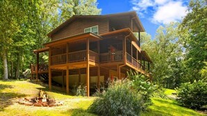 Eine zweistöckige Holzhütte mit Balkon, umgeben von üppigem Grün und einer Feuerstelle.