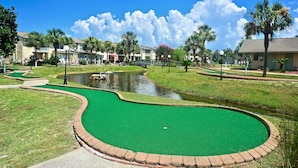 Ein Golfplatz mit Teich, Palmen und einer Brücke.