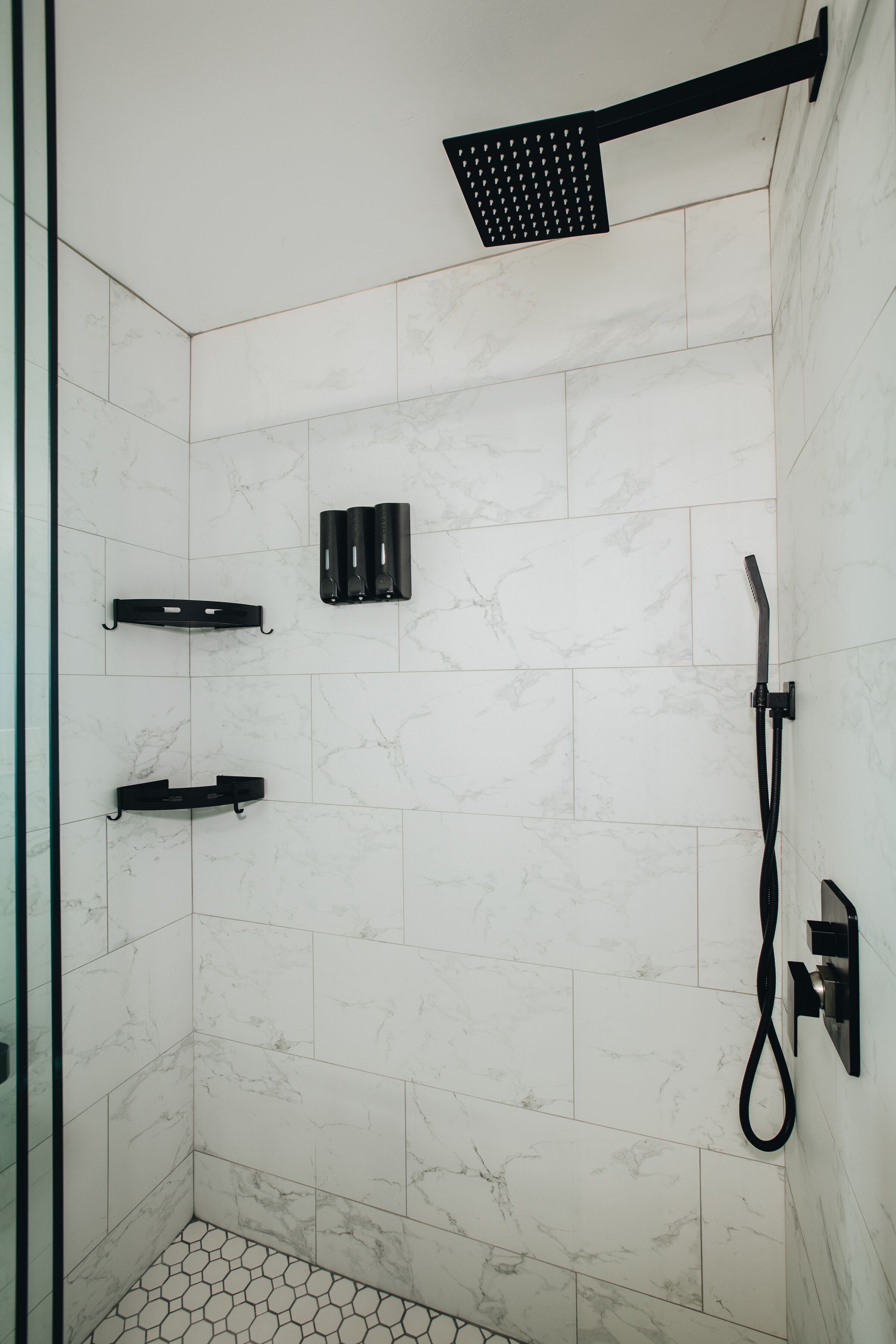 Un área de ducha moderna con ducha de color negro, ducha de mano y grifo empotrado.