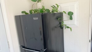 A black refrigerator with a plant on top, next to a stainless steel trash bin in a room with wooden flooring and white walls. - Spacious private studio in Long Beach (Long Beach)
