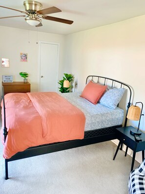 A bedroom with a bed, a ceiling fan, a bedside table with a lamp, and a door.