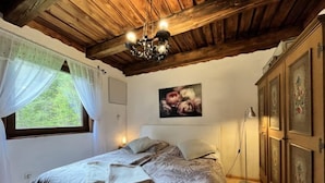 Une chambre avec un plafond en bois, un lit recouvert d’une couvre-lit à motifs, un tableau accroché au mur et une armoire contenant des œuvres d’art.