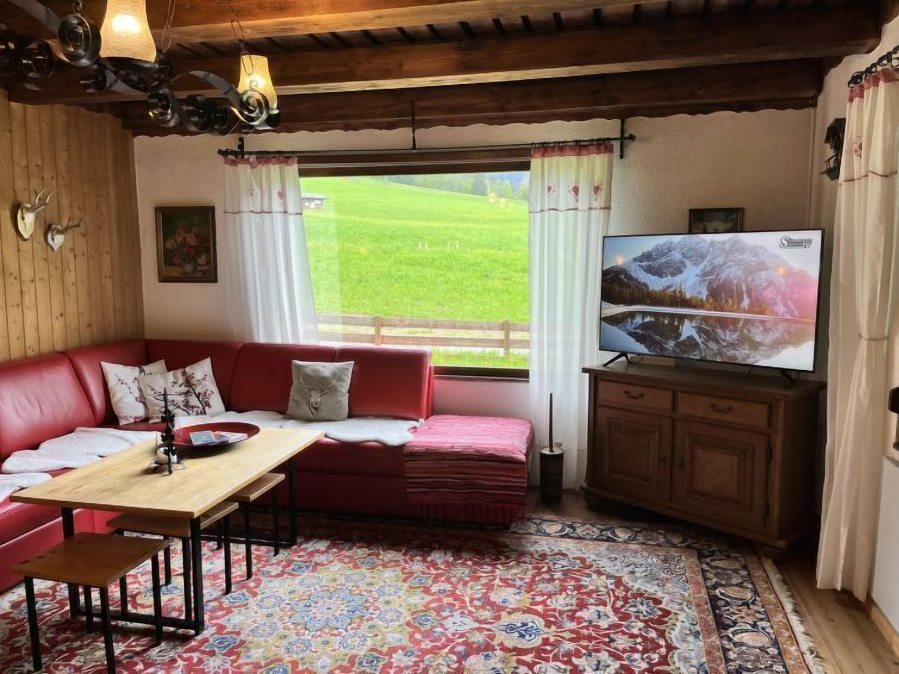 A cozy living room with a red sofa, wooden table, and a television displaying a mountainous landscape.