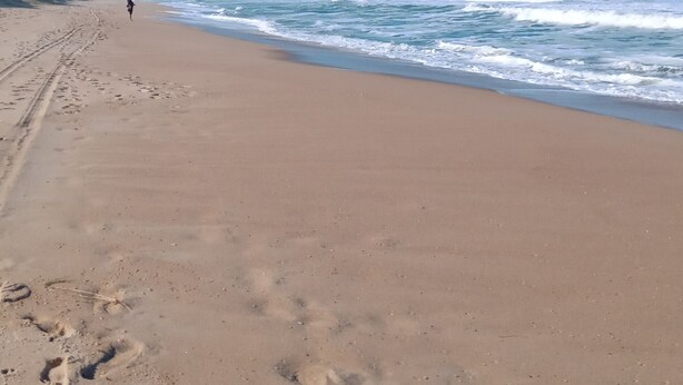 A sandy beach with footprints leading towards the ocean, a clear sky, and distant hills. - Your house in Floripa! (SC)