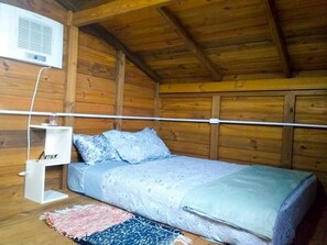 Quarto de cabana de madeira com uma cama, uma estante branca com uma placa de identificação e um aparelho de ar condicionado.