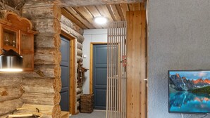 A rustic wooden interior with a television mounted on the wall, a wooden door, and a woven chair.