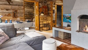 A cozy log cabin interior with a fireplace, a sofa, a dining area, and a television.