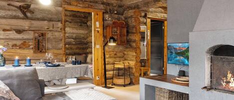 Interior de una cabaña de troncos con sala de estar, una mesa de comedor, chimenea y televisor.