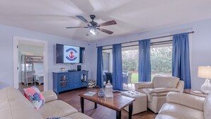 A living room with a ceiling fan, a TV, a blue cabinet, a coffee table, and a sofa. - Better Together @ Edgewater Beach Resort Sleeps 10 (Panama City Beach)