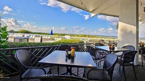 An outdoor patio with tables and chairs, overlooking a scenic view of the ocean and a distant island. - Better Together @ Edgewater Beach Resort Sleeps 10 (Panama City Beach)