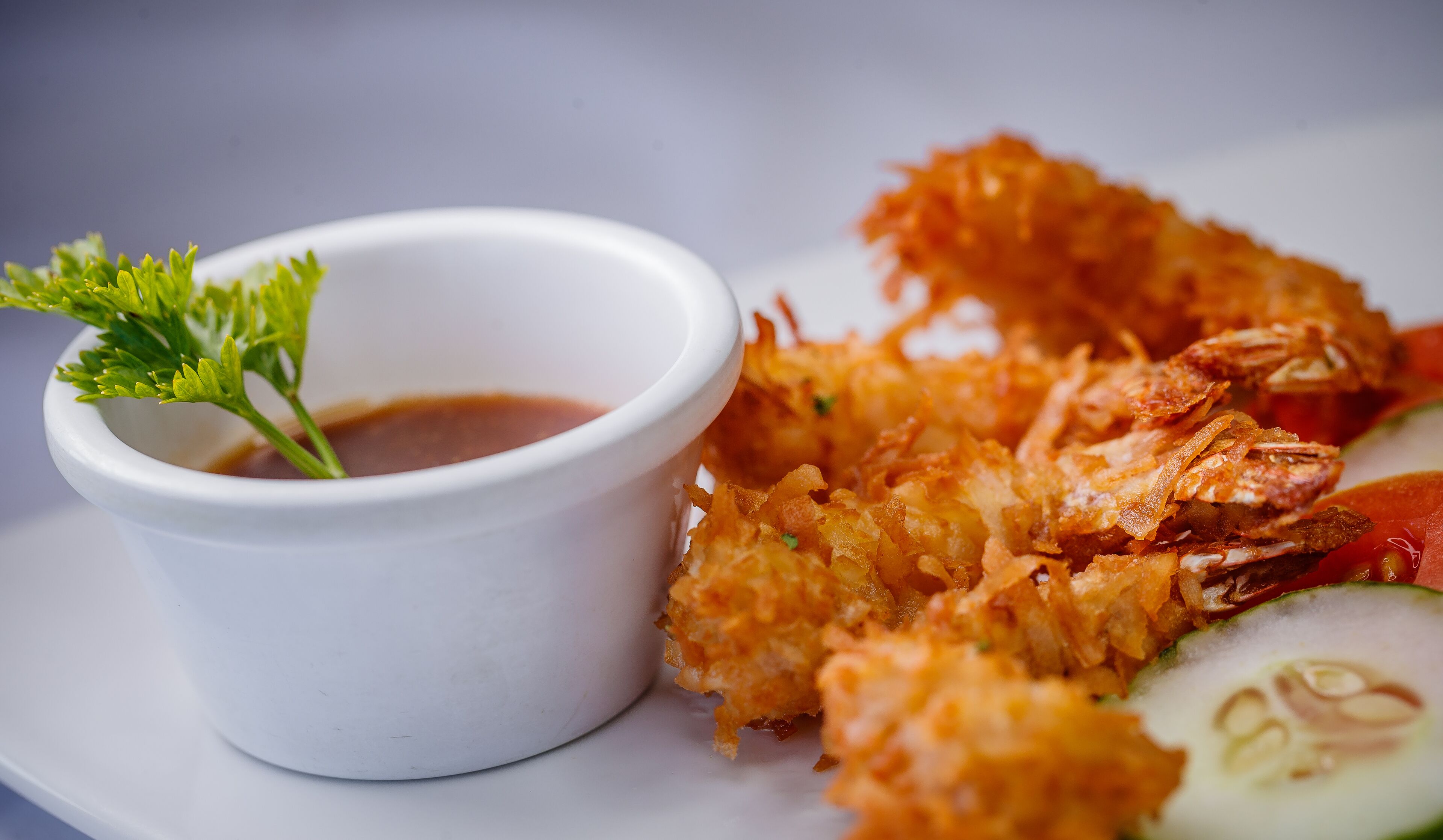 A plate with crispy fried food, a small bowl of dipping sauce, and a garnish of parsley.