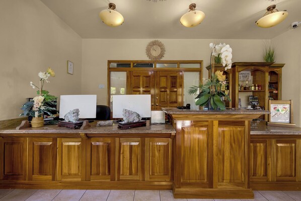 Una cocina con armarios de madera, encimera de mármol y una isla también de madera. Hay dos lámparas colgantes, un reloj y un cuadro en la pared.