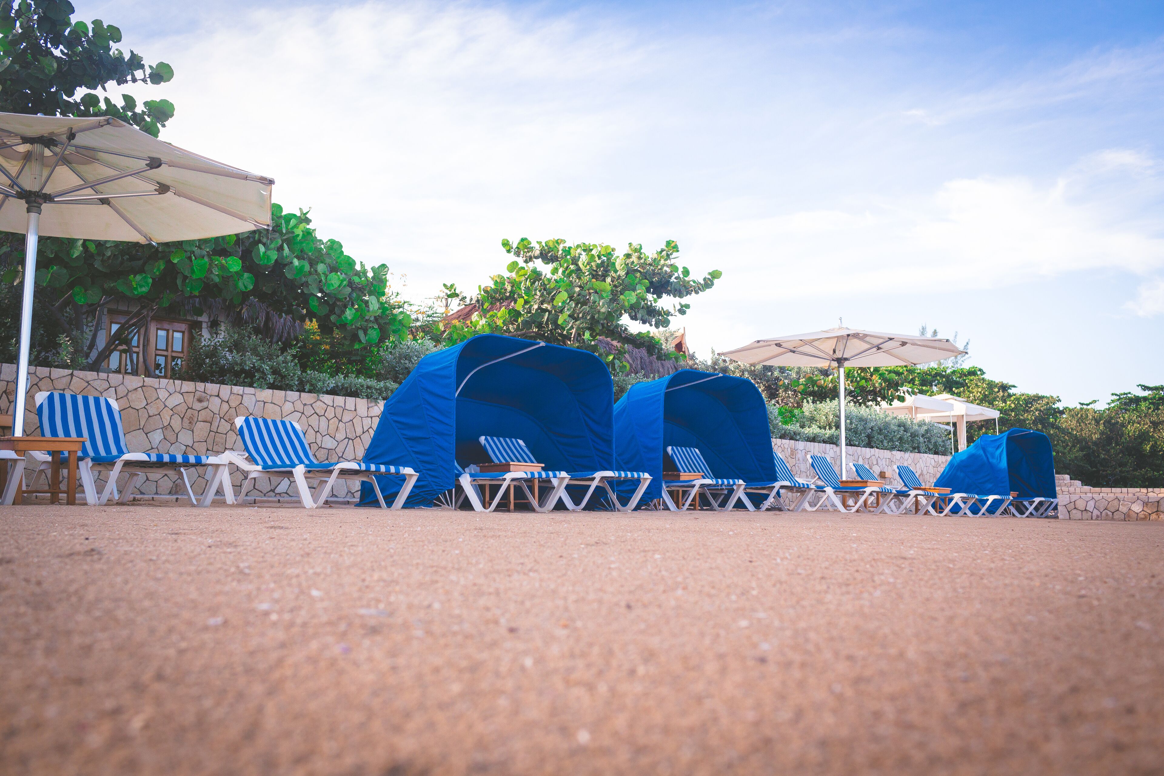 A beachside lounge area with blue and white striped lounge chairs, a stone wall, and a clear sky.