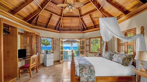 Une chambre avec un plafond en bois, un lit recouvert d’une courtepointe à motifs floraux, un bureau avec un ordinateur et une vue sur la mer.