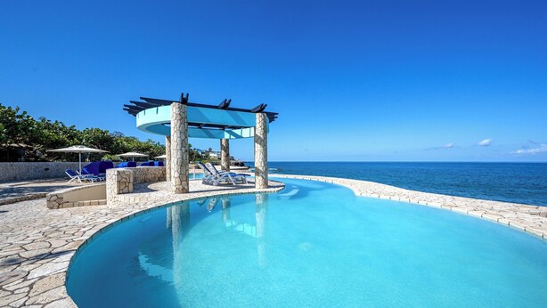 Une piscine d’un bleu éclatant, entourée d’une terrasse en pierre, de chaises longues et agrémentée d’une pergola.