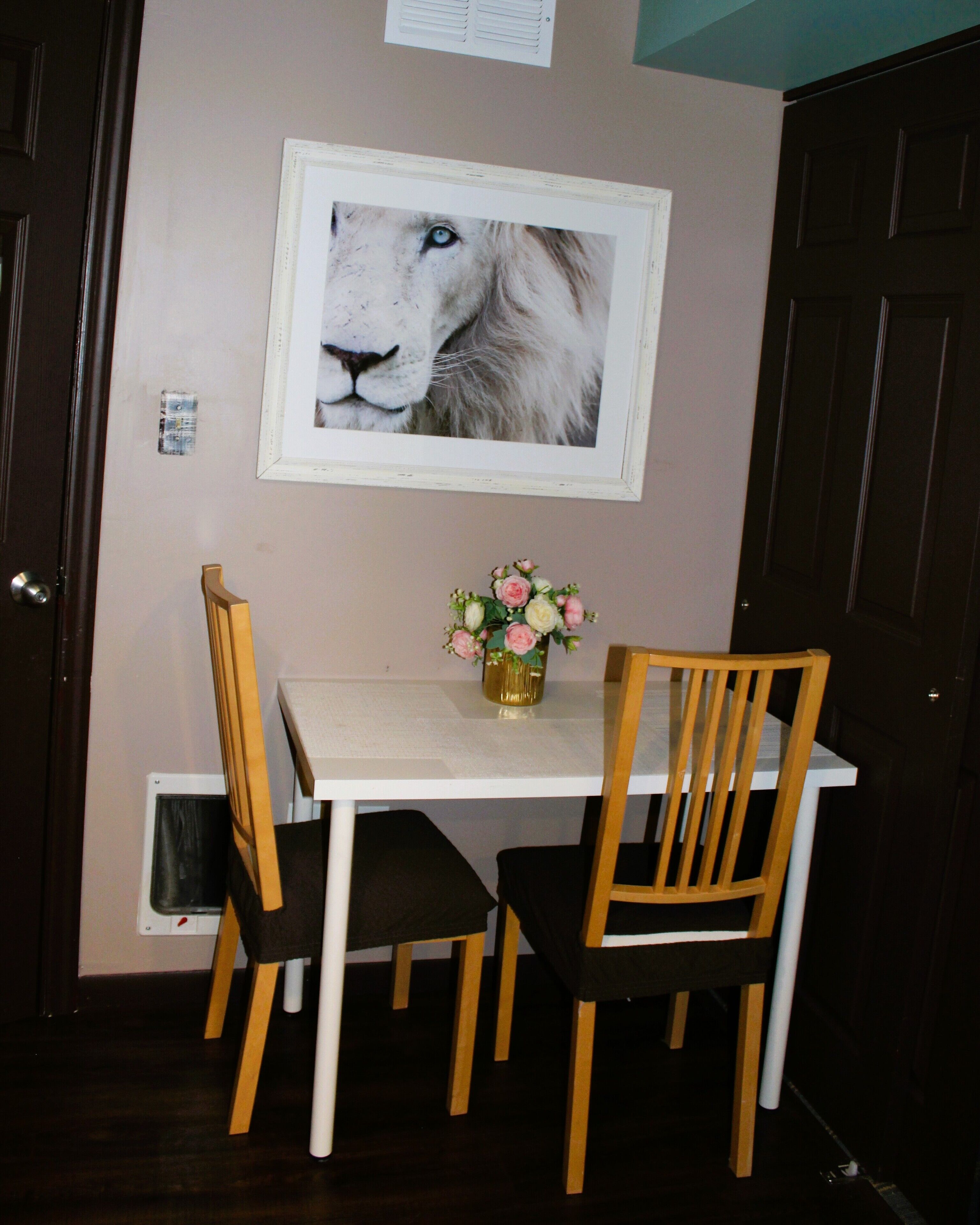 Zona pranzo con tavolo bianco, due sedie di legno e un vaso con fiori.