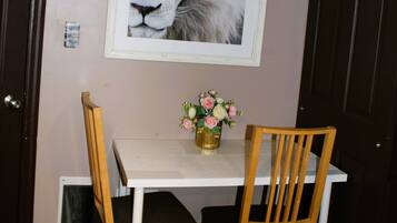 Zona pranzo con tavolo bianco, due sedie di legno e un vaso con fiori.