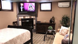 A hotel room with a bed, a sofa, a TV, a fireplace, and a plant. - Comfortable private unit with hot tub, swimming pool and free parking (Gibsonia)