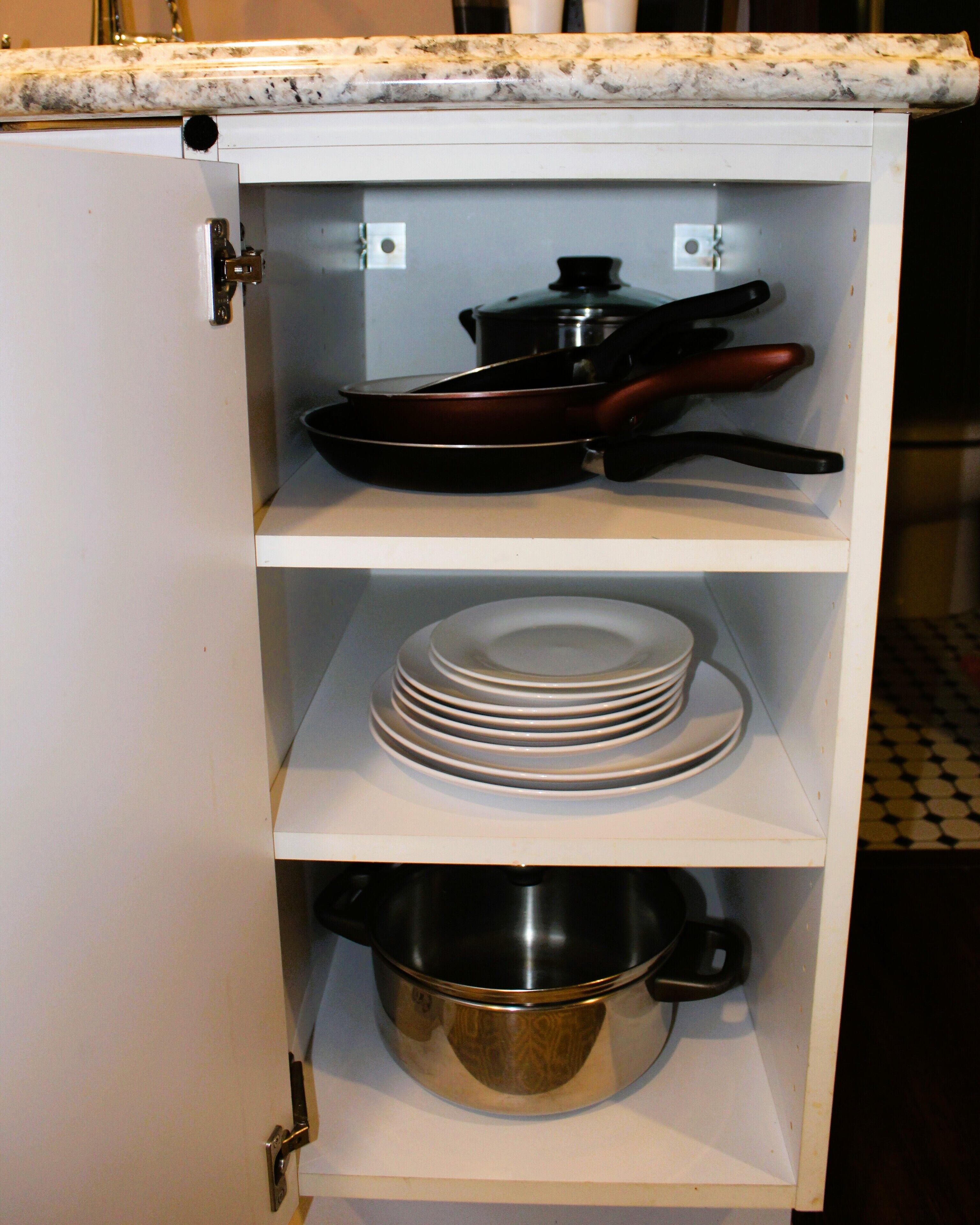Un meuble de cuisine comprenant une plaque de cuisson, une poêle, une pile d’assiettes et une casserole.