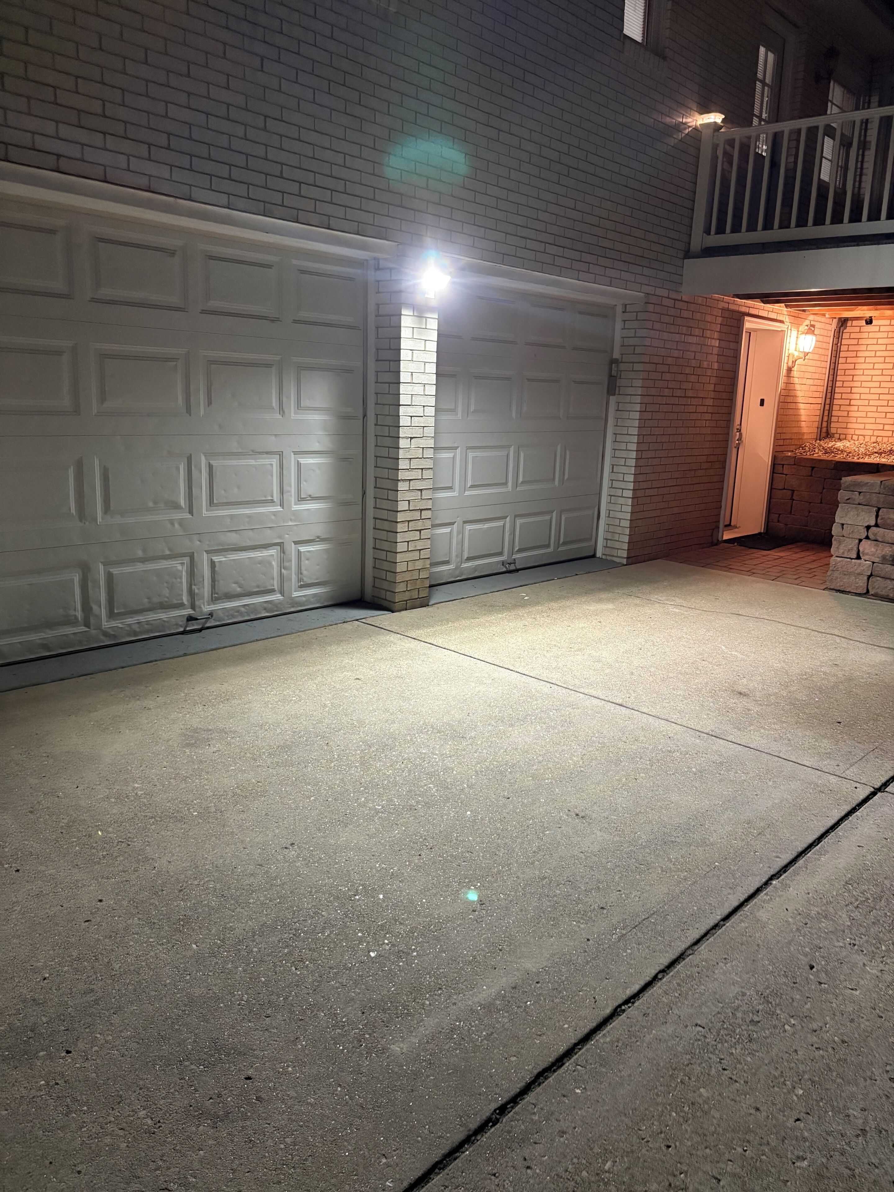 A garage with a white door, a brick pillar, and a concrete driveway.