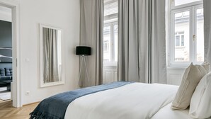 A bedroom with a bed, a floor lamp, and a view of the outside through large windows.
