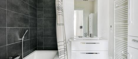 Une salle de bain moderne équipée d’une baignoire, d’une douche et d’un meuble-lavabo avec un miroir.