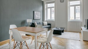 A modern living room with a dining table, white chairs, a grey sofa, and a black coffee table.